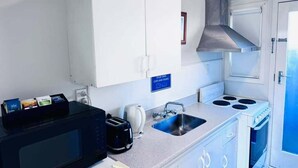 Une cuisine compacte avec des meubles blancs, une hotte en acier inoxydable, un four à micro-ondes, un grille-pain et un évier.