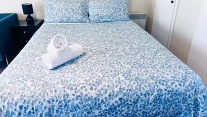 A neatly made bed with a floral-patterned bedspread, a rolled white towel, and a bedside lamp on a nightstand.