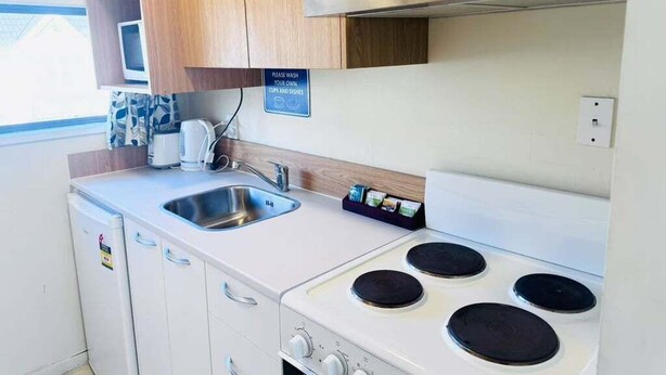 A compact kitchenette with a stove, sink, and wooden cabinets.