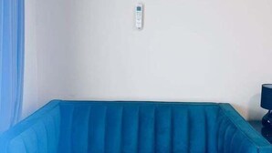 A room with a blue sofa, an air conditioning unit mounted on the wall, and a remote control on the floor.