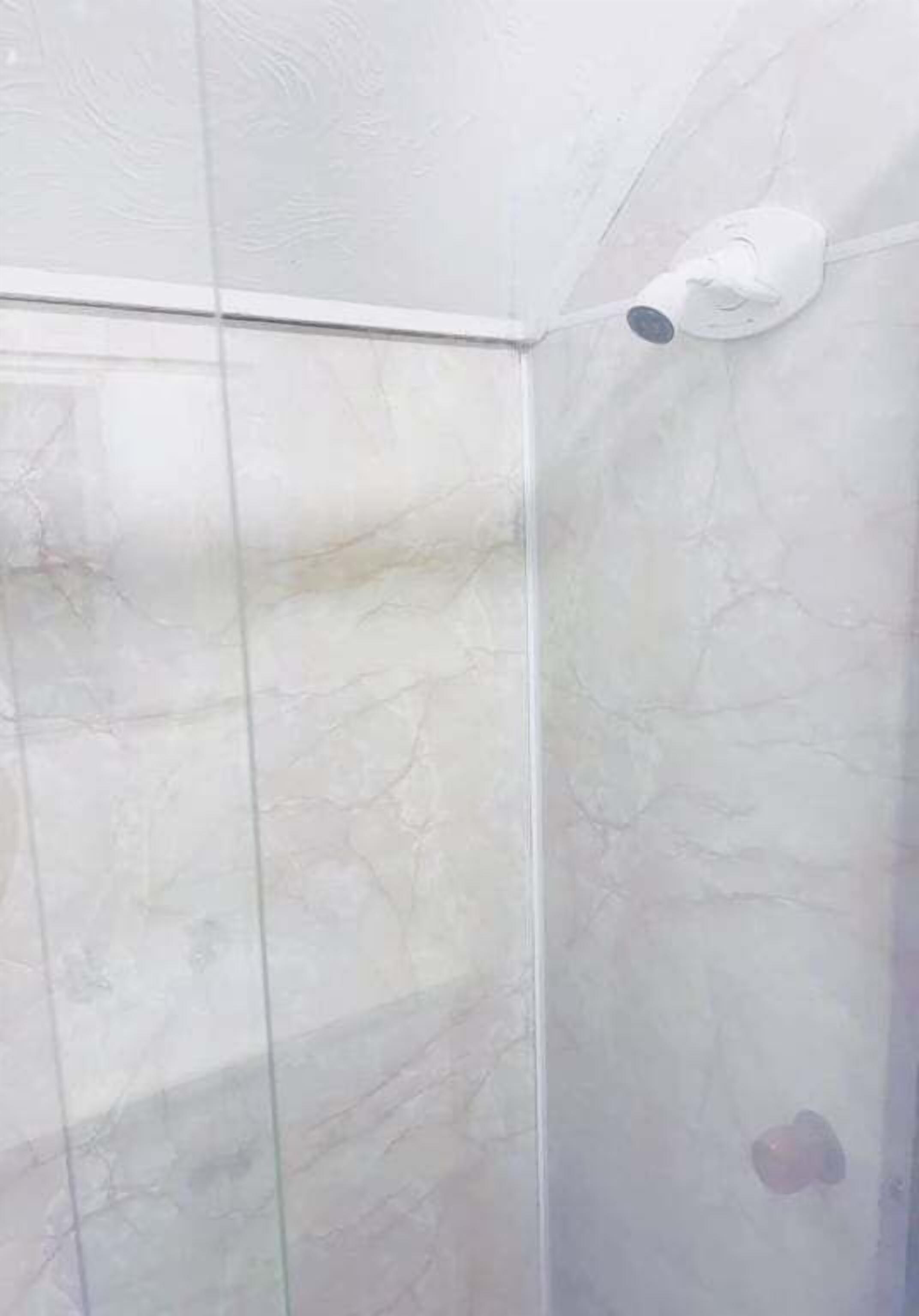 A bathroom with a white marble wall, a white ceiling, and a white showerhead.