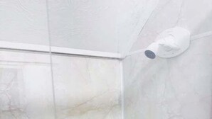 A bathroom with a white marble wall, a white ceiling, and a white showerhead.