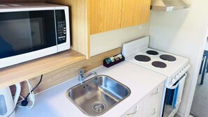 A compact kitchenette with a microwave, stove, sink, and wooden cabinets.