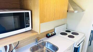 A compact kitchenette with a microwave, stove, sink, and wooden cabinets.