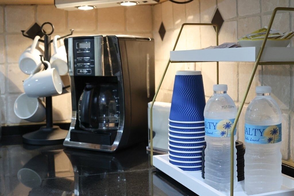A coffee machine, stacked cups, and water bottles on a counter.