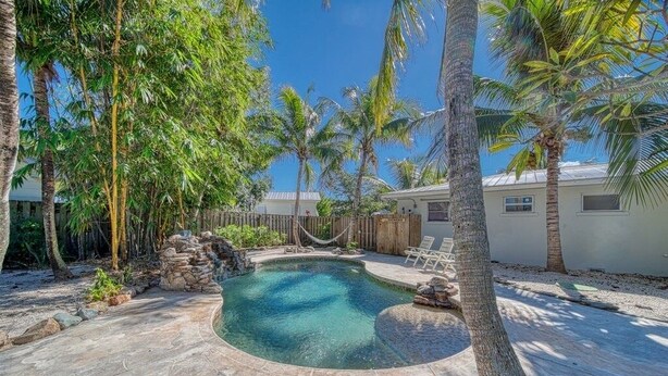 A circular pool with a stone edge, surrounded by palm trees and a wooden fence. - Tropical Retreat • Pool • 1.5 miles to Beach (Hobe Sound)