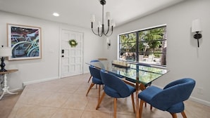 A dining area with a glass table, blue chairs, a chandelier, and a view of the outdoors. - Tropical Retreat • Pool • 1.5 miles to Beach (Hobe Sound)