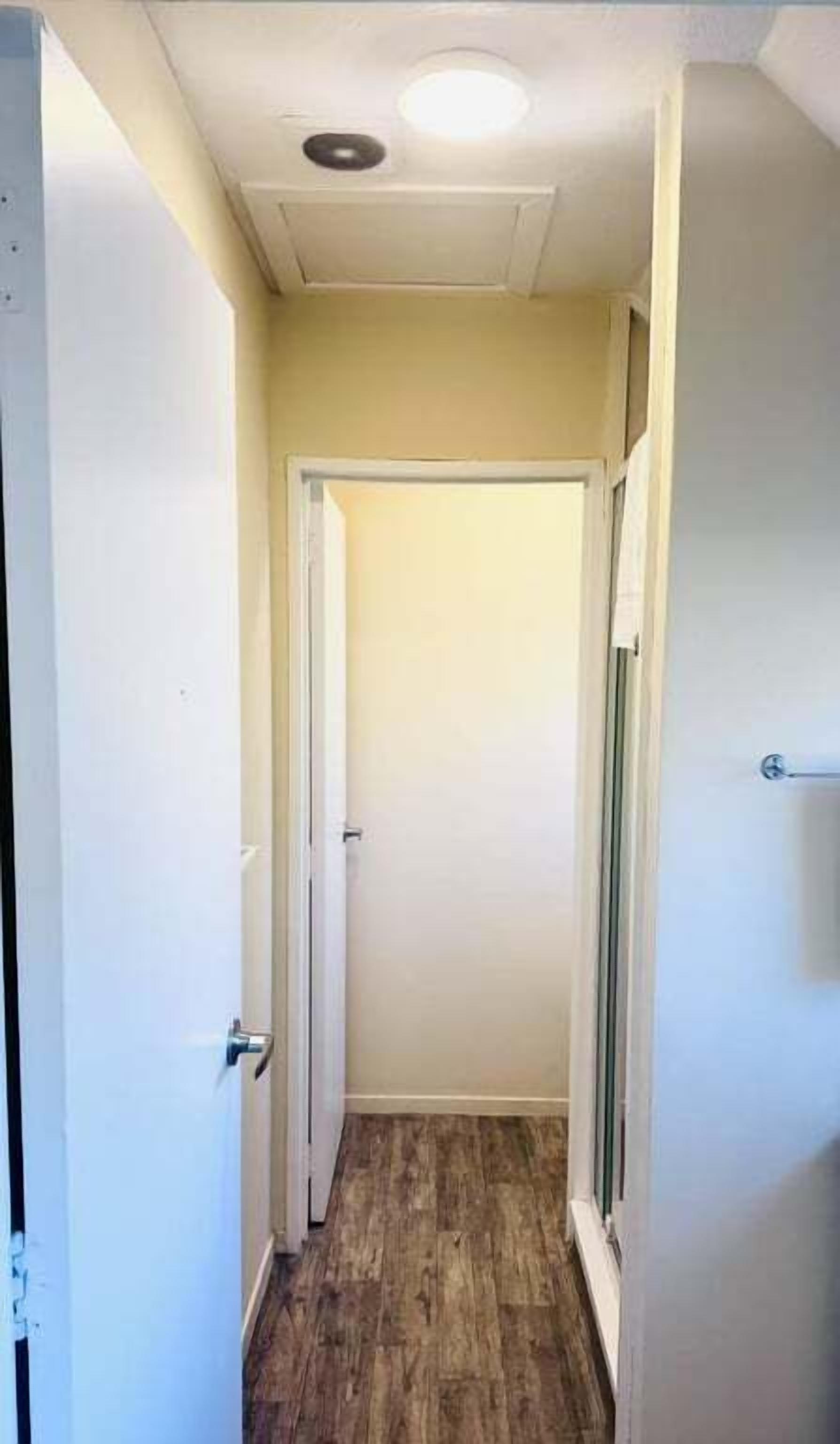 A narrow hallway with wooden flooring, white walls, and a door at the end.