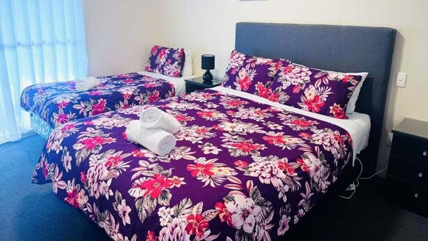 Une chambre d’hôtel avec deux lits, chacun recouvert d’une couvre-lit à motifs floraux, une table de chevet avec une lampe et deux tableaux encadrés accrochés au mur.