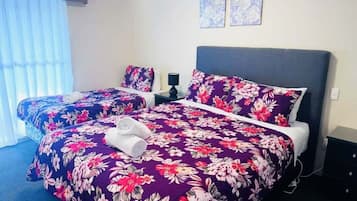 A hotel room with two beds, each with a floral bedspread, a nightstand with a lamp, and two framed pictures on the wall.