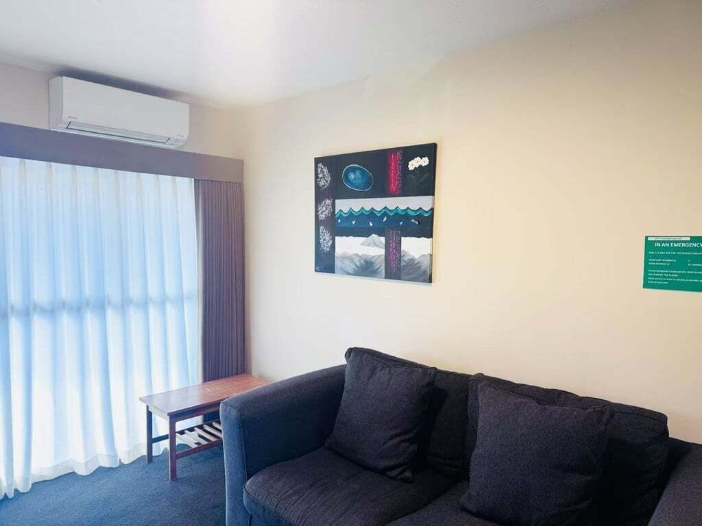 A room with a dark-colored sofa, a small wooden table, and a large window with sheer curtains.
