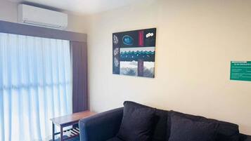 A room with a dark-colored sofa, a small wooden table, and a large window with sheer curtains.