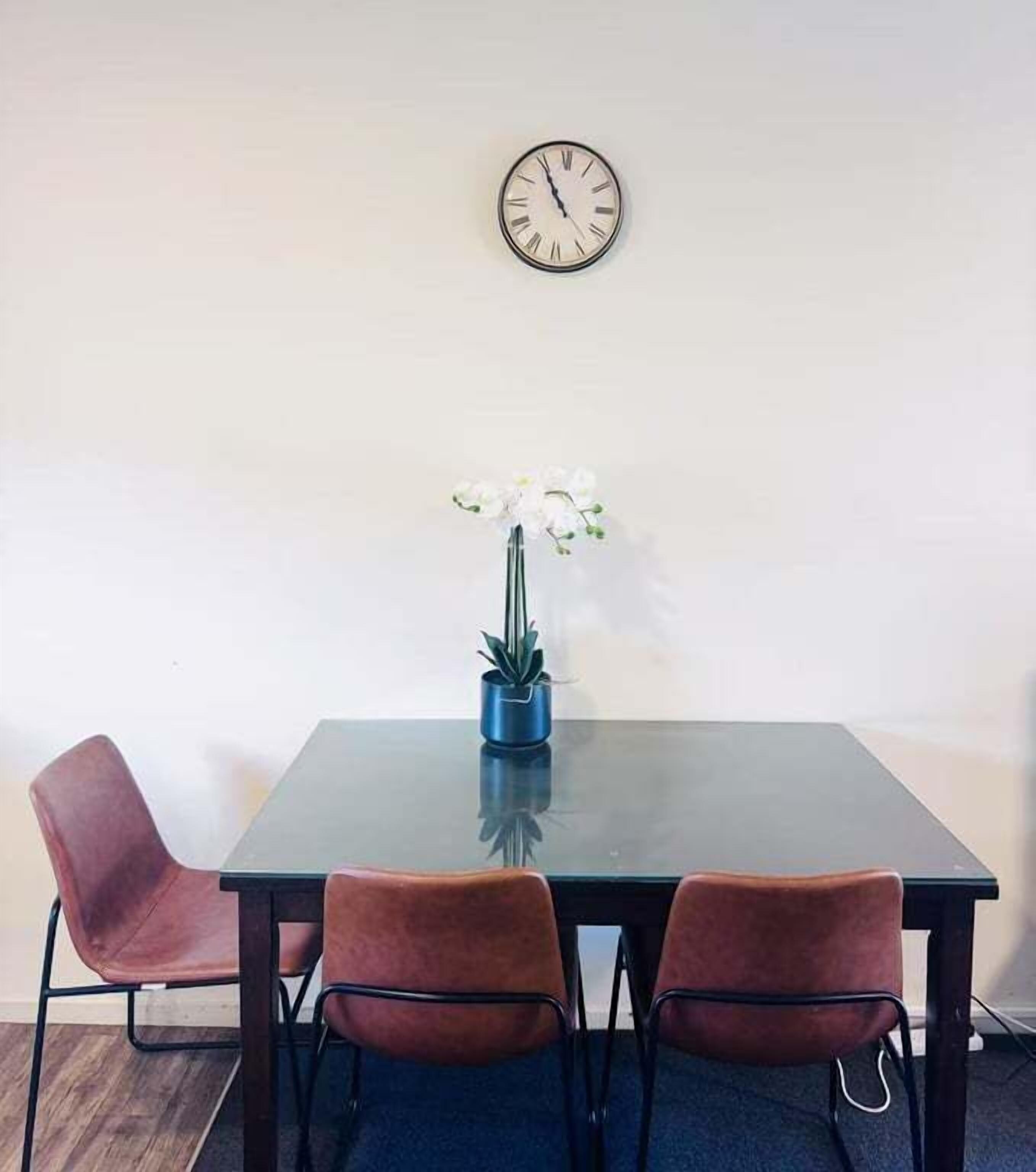 A table with a clock, two chairs, and a potted plant.