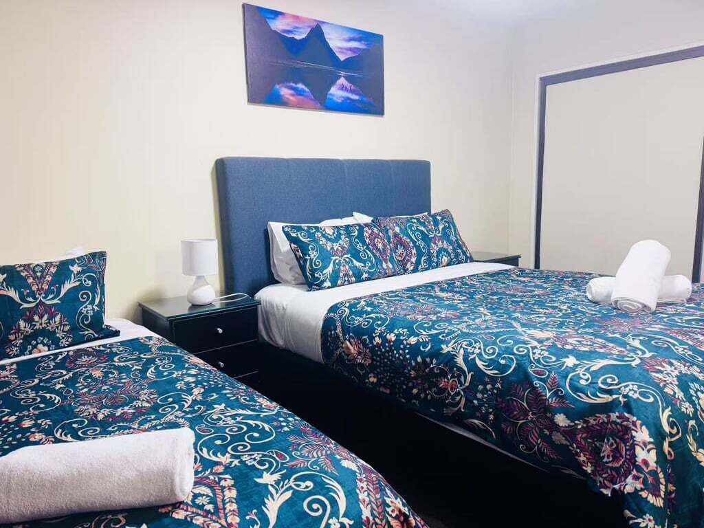 A hotel room with two beds, each with a patterned bedspread, a nightstand with a lamp, and a wall-mounted artwork.