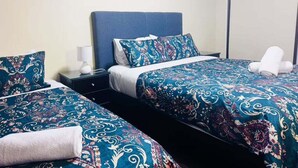 A hotel room with two beds, each with a patterned bedspread, a nightstand with a lamp, and a wall-mounted artwork.