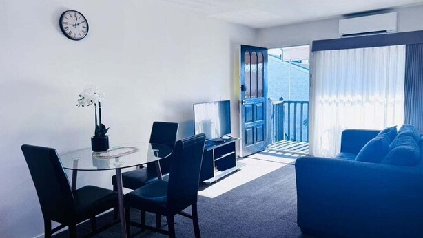 A modern living room with a glass dining table, blue sofa, and a view of the outside.