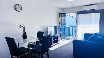 A modern living room with a glass dining table, blue sofa, and a view of the outside.