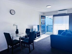 Ein modernes Wohnzimmer mit einem Glastisch, einem blauen Sofa und Blick ins Freie.