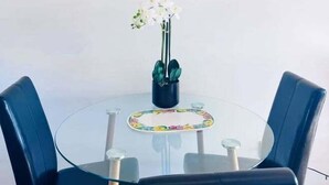 A round glass table with four blue chairs, a clock on the wall, and a potted plant with white flowers.