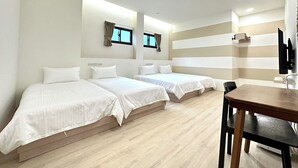 Une chambre d’hôtel avec trois lits simples, un plancher en bois, un bureau avec une chaise et un téléviseur fixé au mur.