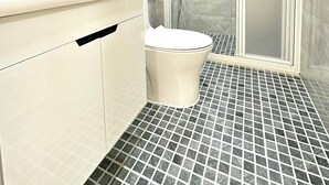 Une salle de bain moderne avec des toilettes blanches, une douche à parois de verre et un sol carrelé.