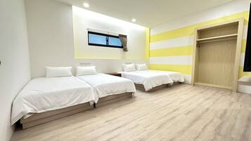 A hotel room with two single beds, a wooden floor, a window with curtains, and a wardrobe.