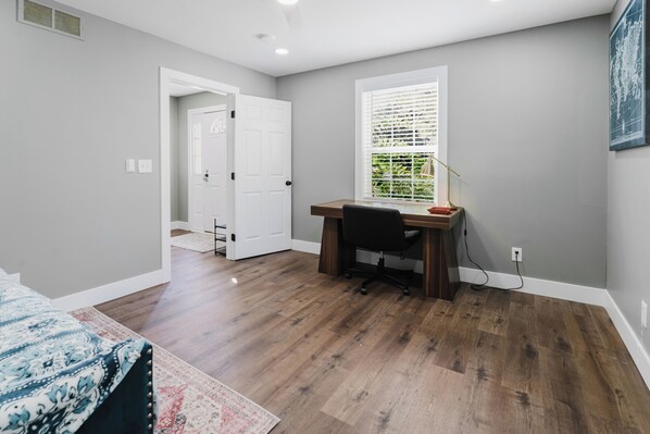 Un dormitorio con piso de madera, un escritorio, una silla y una ventana con persianas.