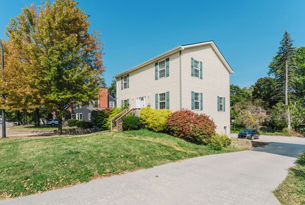 A two-story residential building with a front yard, a driveway, and a parked car.