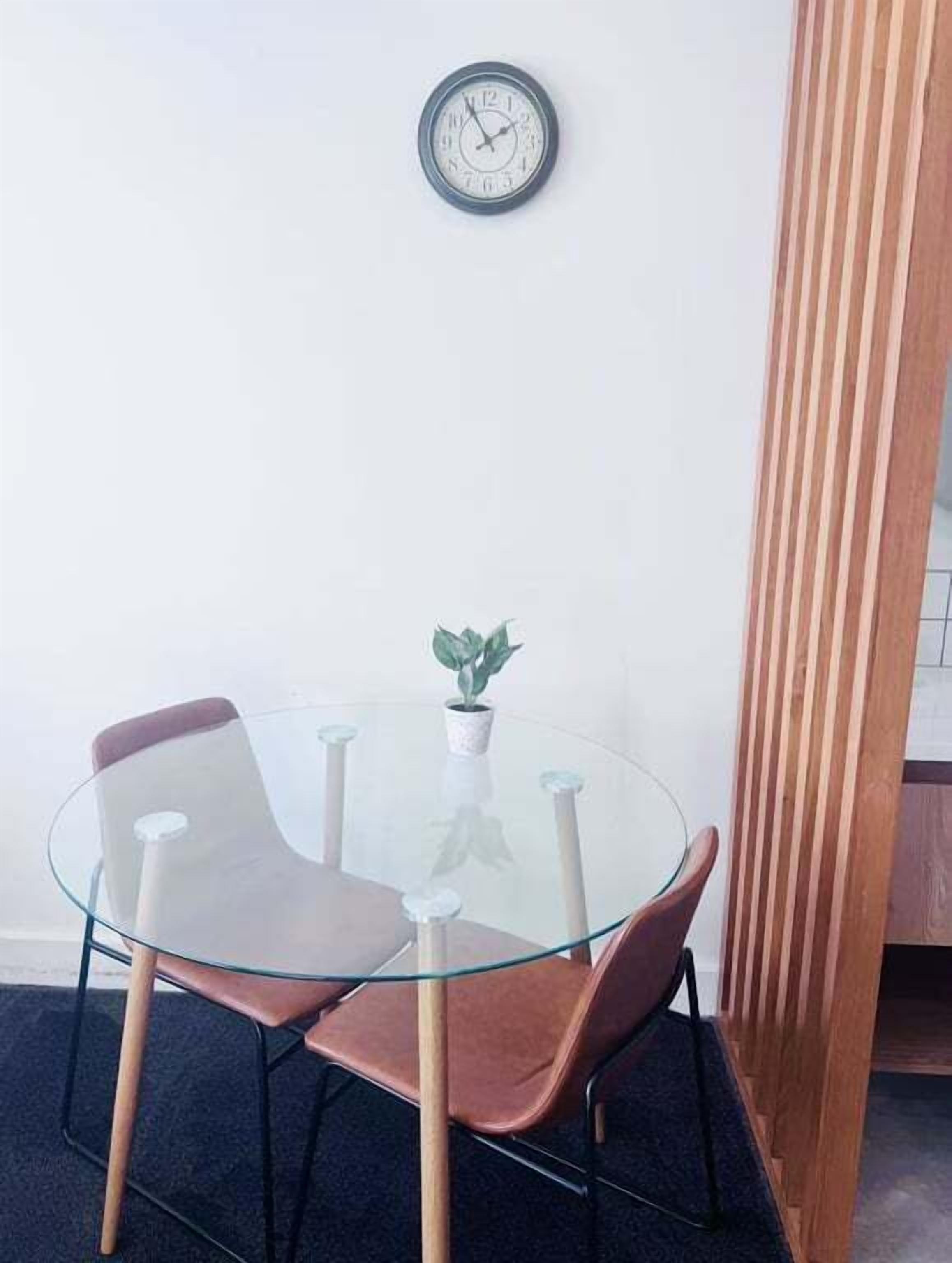 A glass-top table with two chairs, a potted plant, and a wall clock.