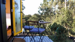 A deck with a folding chair and a small table, surrounded by greenery.