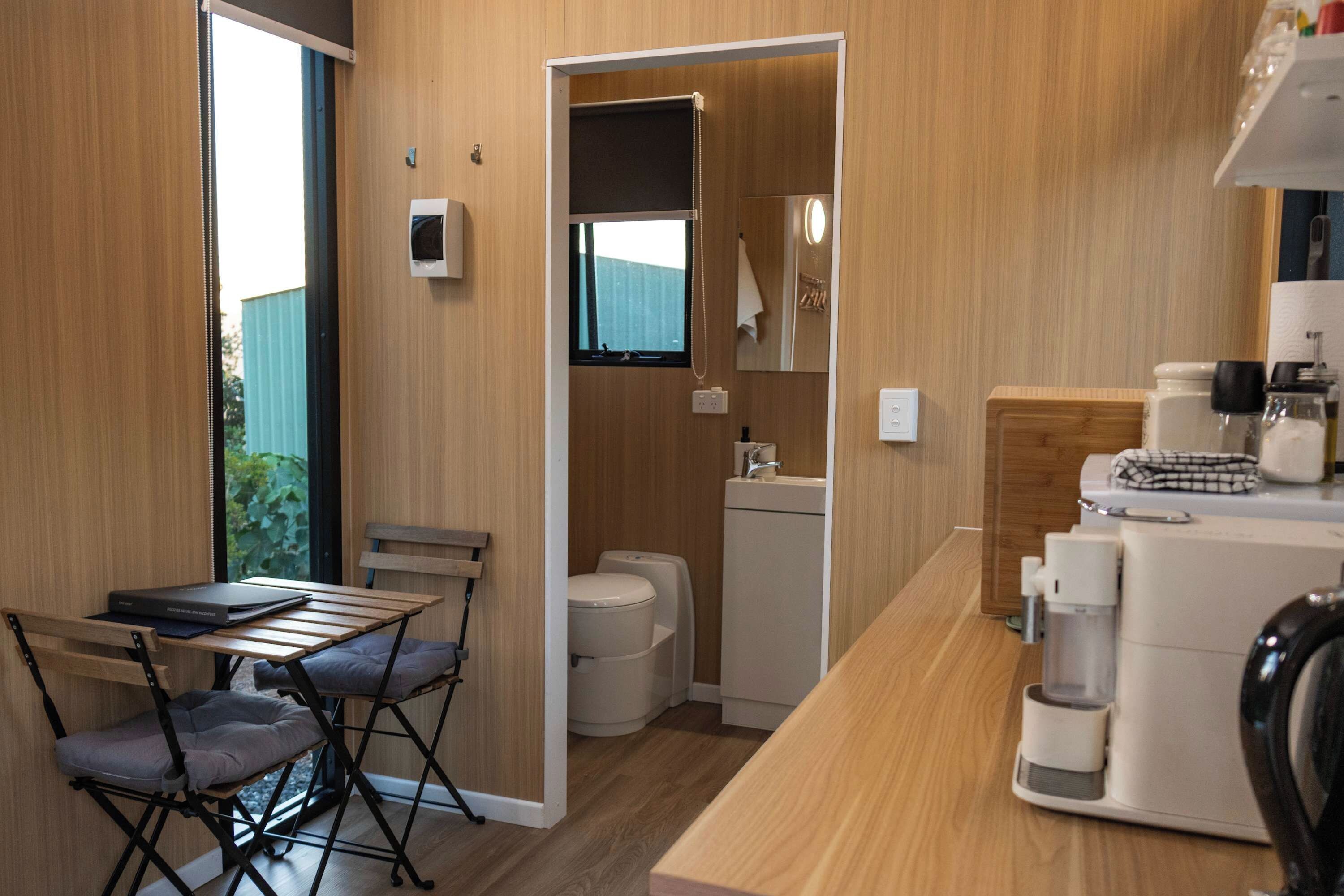 A compact kitchenette with a sink, a coffee machine, and a small table with a chair.