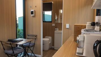 A compact kitchenette with a sink, a coffee machine, and a small table with a chair.