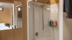 A modern bathroom with a glass-enclosed shower, a mirror, and a shelf with toiletries.