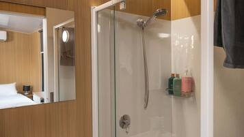 A modern bathroom with a glass-enclosed shower, a mirror, and a shelf with toiletries.