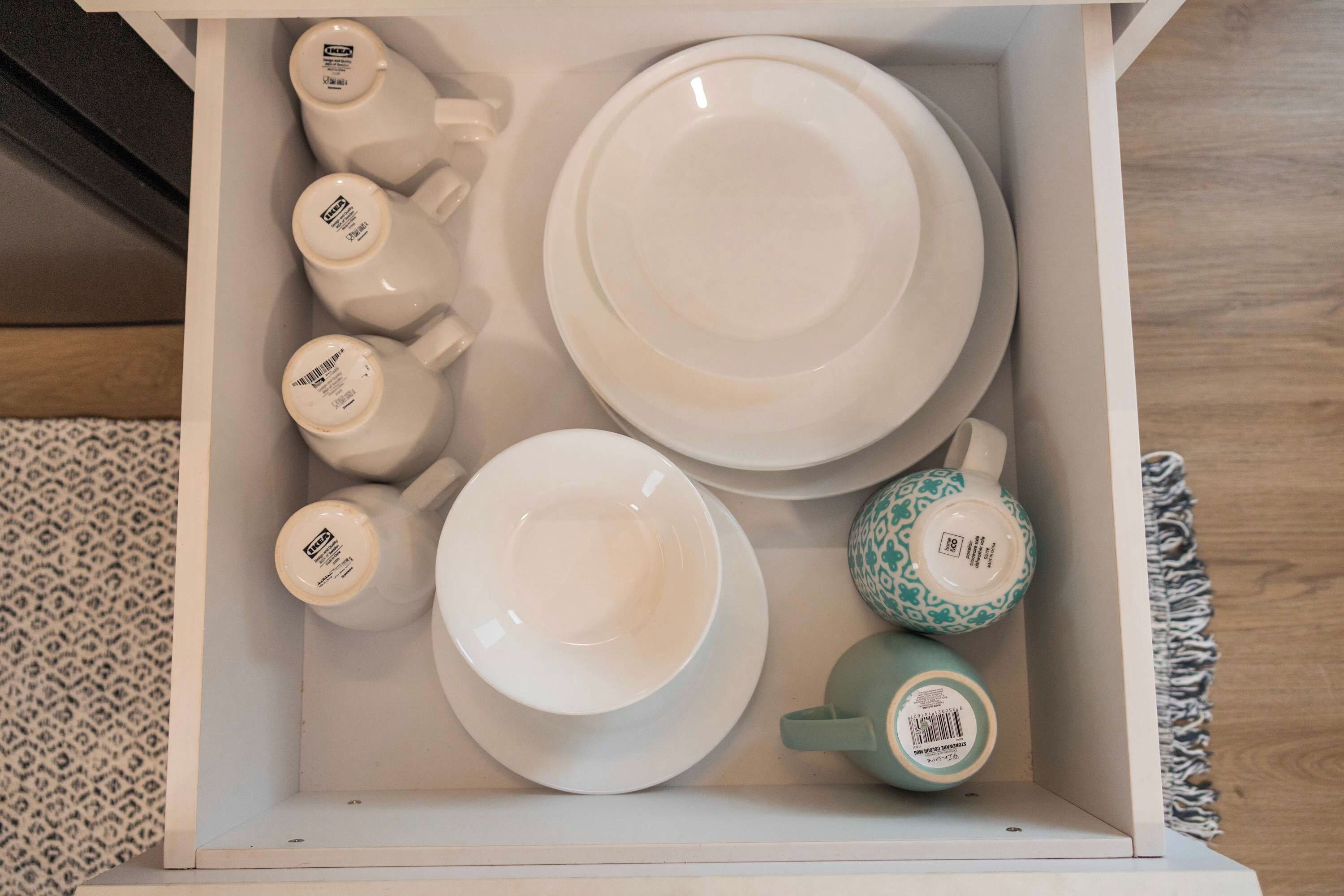A white storage box containing various white ceramic tableware items including plates, cups, and a teapot.