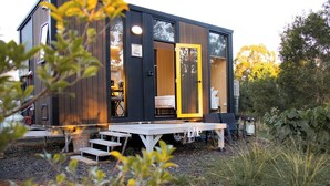 A modern, compact cabin with a large sliding door, a small deck, and a visible kitchen area.