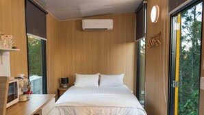 A bedroom with a bed, bedside table, lamp, and an air conditioning unit.