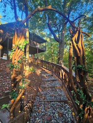 Une terrasse en bois avec une rambarde, entourĂ©e dâarbres et bordĂ©e par un bĂątiment dotĂ© dâun balcon.