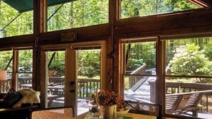 Un interior de madera con ventanas amplias, una mesa con un jarrón de flores y vista a una terraza exterior.