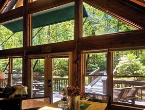 En inredning med trädetaljer, stora fönster, ett bord med en vas med blommor och utsikt över en utomhusveranda.