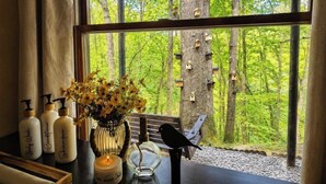 Una habitación con un ventanal grande, vigas de madera, un banco y casas de pájaros afuera.
