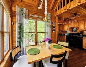LâintĂ©rieur dâun chalet en bois comprend une table Ă manger, des chaises, un coin cuisine et offre une vue sur lâextĂ©rieur.