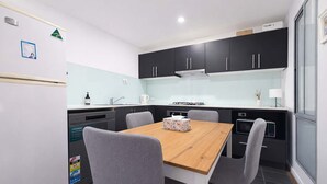 A modern kitchen with a wooden table and grey chairs, a dishwasher, and black cabinets. - Stylish 2BR Brunswick Home (Brunswick)