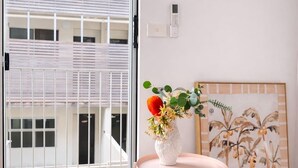 A room with a large window, a small round table with a vase of flowers, a bed with an orange blanket, and a framed picture on the wall. - Stylish 2BR Brunswick Home (Brunswick)