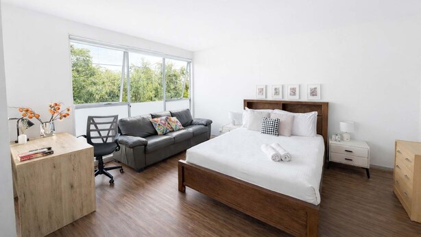 A modern bedroom with a large bed, a desk, a chair, and a sofa. - Stylish 2BR Brunswick Home (Brunswick)