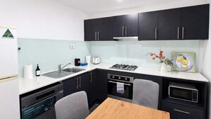 A compact kitchen with black cabinets, a sink, a stove, a microwave, and a dining area with a table and chairs. - Stylish 2BR Brunswick Home (Brunswick)