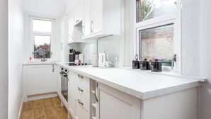 A modern kitchen with white cabinetry, a marble countertop, and a window with a view of a brick building. - The Bay Suite - Donnini Apartments (Troon)