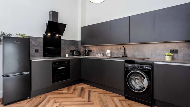 Une cuisine moderne avec des meubles de rangement aux couleurs sombres, un four encastré, un lave-vaisselle et un lave-linge.
