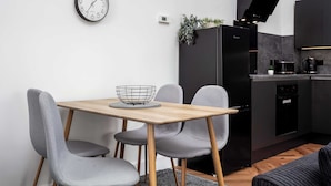 Une cuisine moderne avec un réfrigérateur noir, une machine à café et un four à micro-ondes. On y trouve une table à manger avec deux chaises et une petite plante accrochée au mur.