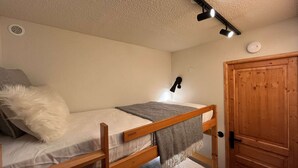 A bunk bed with a headboard, a bedside lamp, a wooden door, and a wall-mounted light fixture. - Newly renovated slopeside studio (Montchavin-les-coches)
